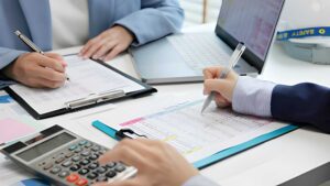Professional bookkeeper reviewing financial records, invoices, and business reports while using accounting software in a modern office.